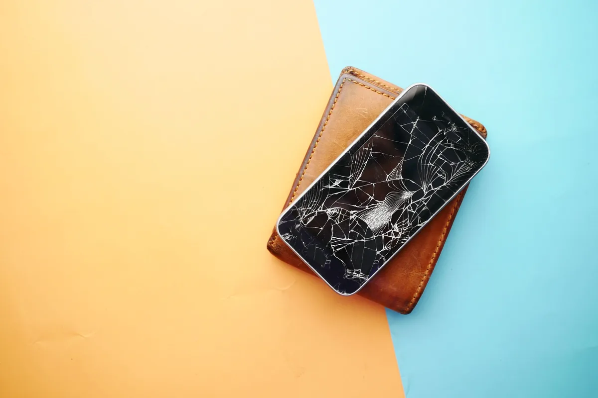 Smartphone mit gesprungenem Display liegt auf einer Brieftasche