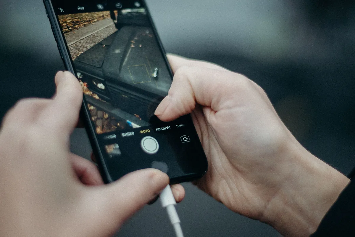 Smartphone in beiden H&auml;nden gehalten, wei&szlig;es Ladekabel eingesteckt
